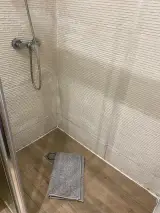 Corner of the shower with mixer tap and folded grey towel on the floor in the Interior Apartment bathroom
